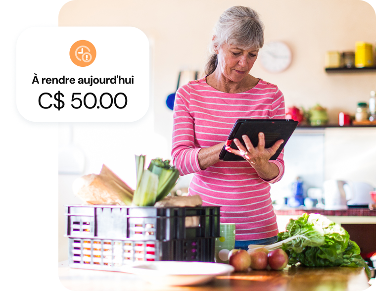 Une femme âgée gère son budget sur une tablette, à côté d'un panier de produits frais.