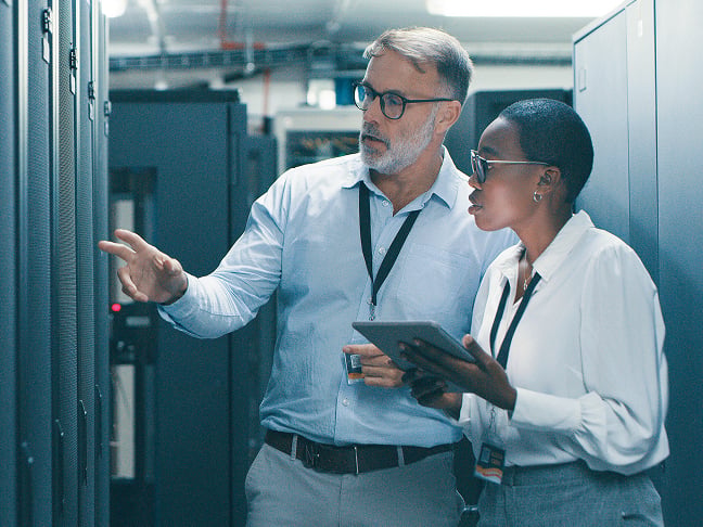 Man and woman in mainframe room talking and looking at tablet