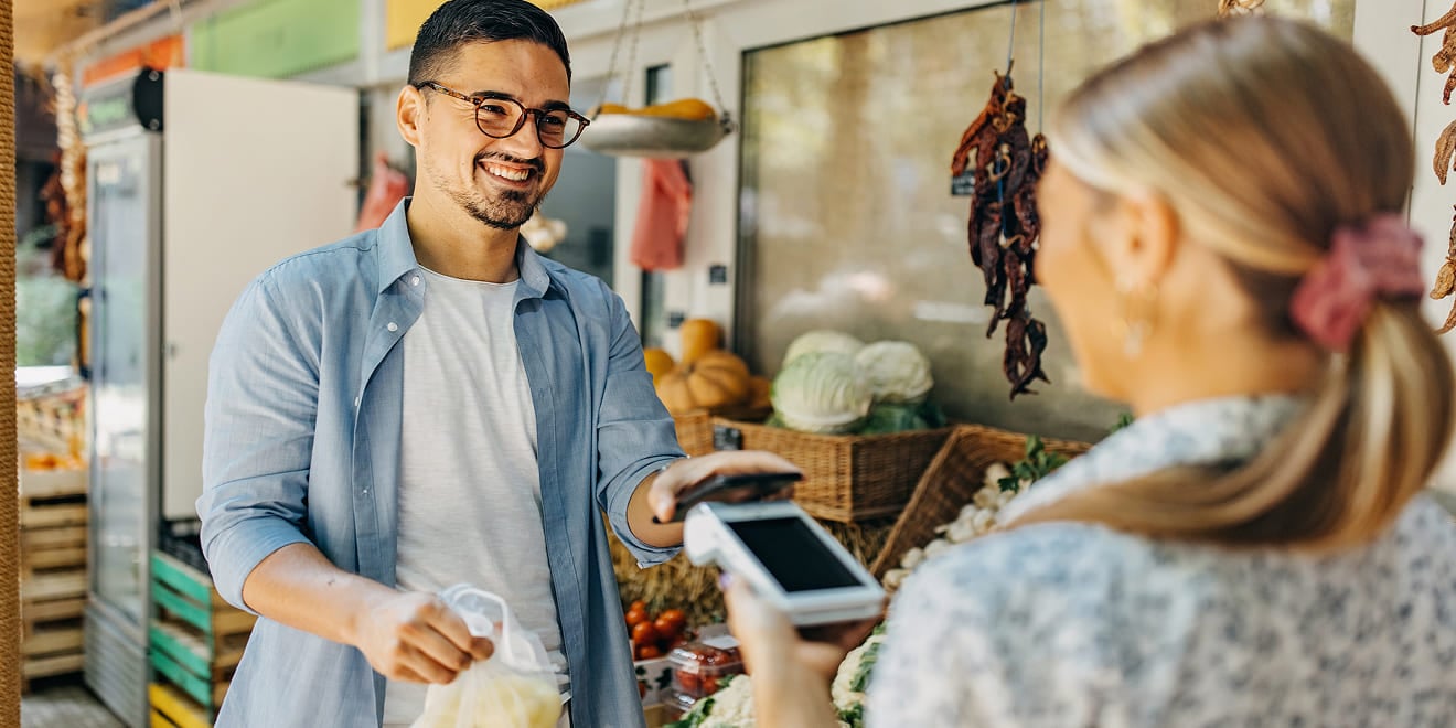 Man tapping his smartphone on a card terminal to buy produce at an outdoor market.