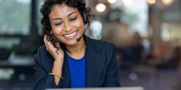 Woman with curly hair smiling while taking a phone call with a headset.