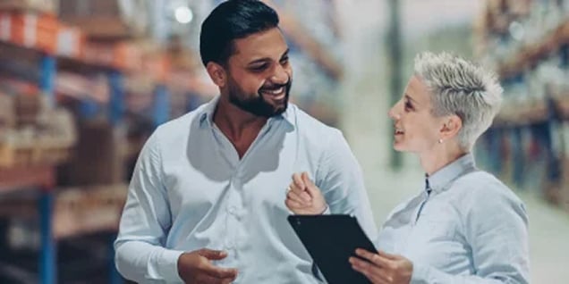 Woman holding a tablet while discussing inventory with a male colleague in a warehouse.