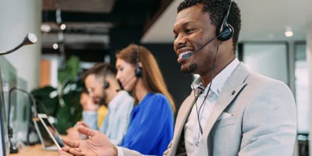 Man wearing a headset gesturing while taking a customer support call at his desk.
