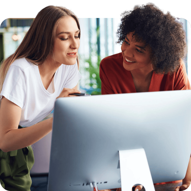 Two women in an office looking at a desktop monitor while collaborating.