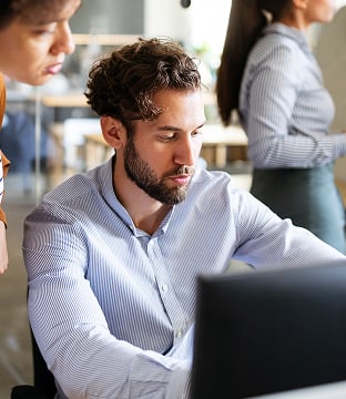 A man works at a computer, as his manager leans over him checking his work.
