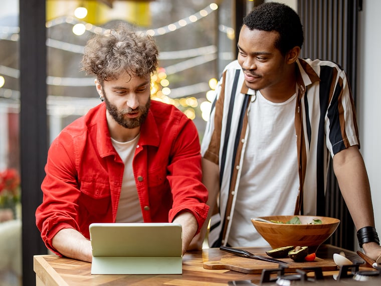 Two men in a restaurant lean over a tablet.