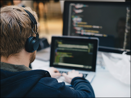 A visual showing someone from behind wearing headphones sitting at a laptop.