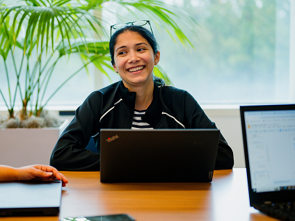 A smiling woman sits at a desk with her laptop.