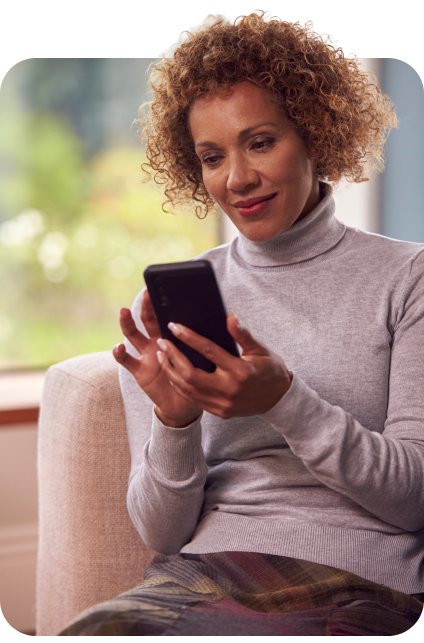 A smiling person wearing a turtleneck sweater uses their smart phone.