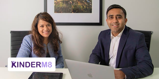 Man and woman smiling in office setting while looking at laptop computer on desk