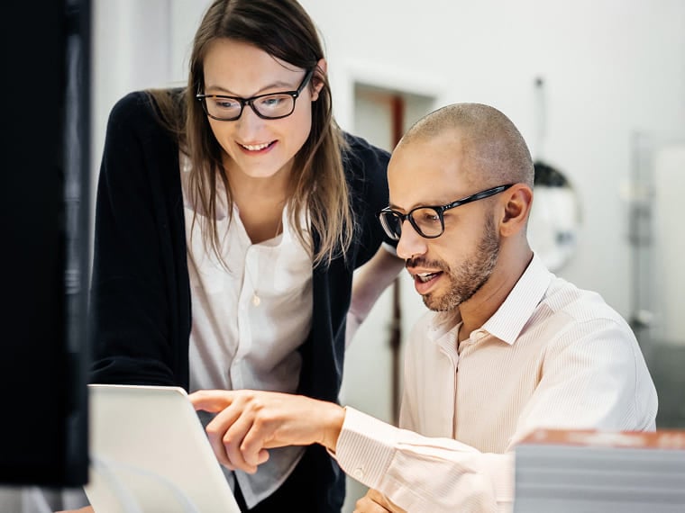 Male and female office workers with glasses collaborating at a computer.