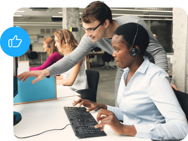 Male colleague assisting a call center representative at her workstation desk.
