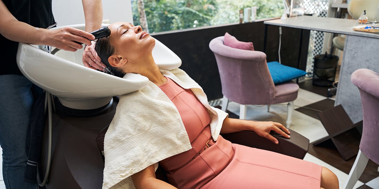 Une employée de salon rince les cheveux d'une cliente à un bac à shampoing.