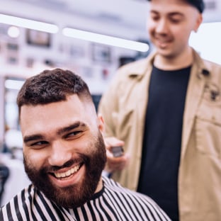 A barber cutting a smiling customer’s hair in a barbershop.