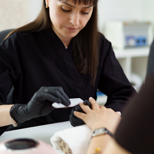 Une technicienne lime les ongles d'une cliente à un poste de travail dans un salon de beauté.