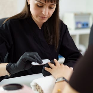 A technician filing a customer’s fingernails at a salon workstation.