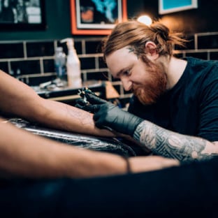 Un tatoueur applique de l'encre sur l'avant-bras d'un client dans un studio de tatouage.