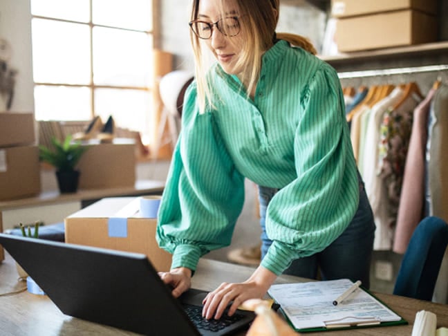 Woman with glasses using a laptop while managing orders in a boutique workspace