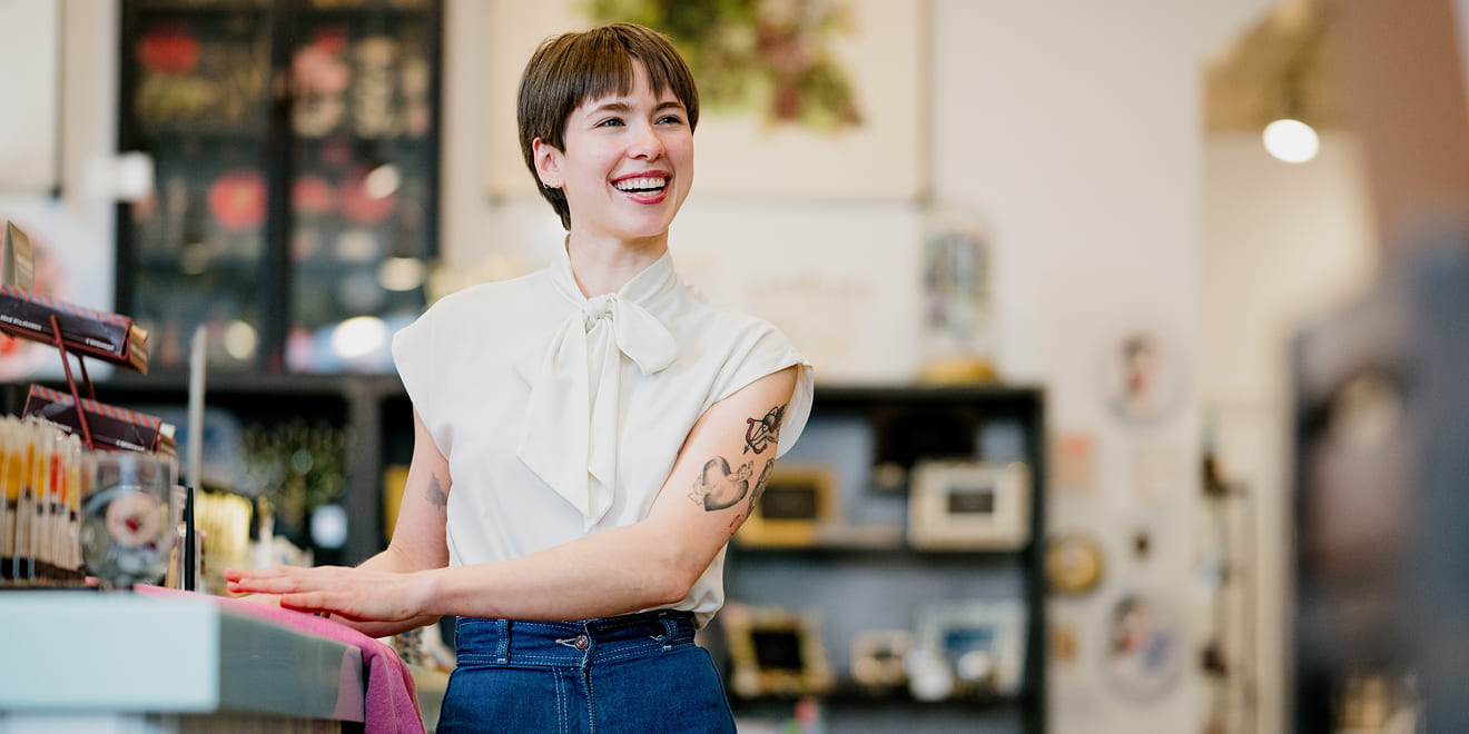 A woman with short hair and arm tattoos smiling warmly at a customer
