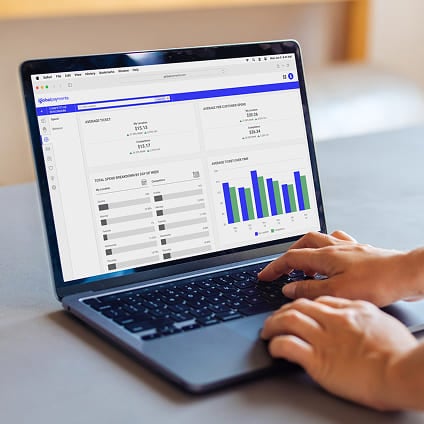 Person typing on a laptop screen showing business reporting metrics and graphs.