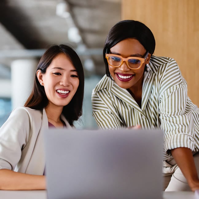 Two smiling businesswomen collaborating while looking at a laptop computer.