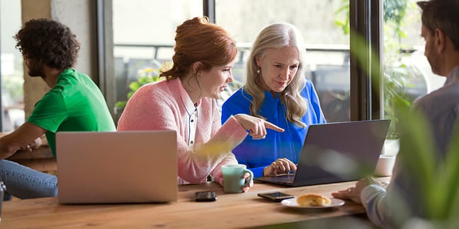 Two women collaborating on a project using a laptop at a shared table
