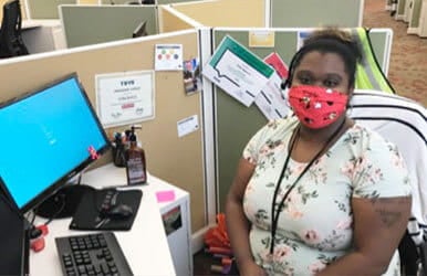 Woman wearing a red face mask sitting at an office cubicle desk.