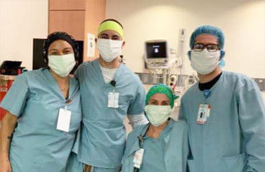 Quatre professionnels de santé en tenue de protection posant ensemble dans une chambre d'hôpital.