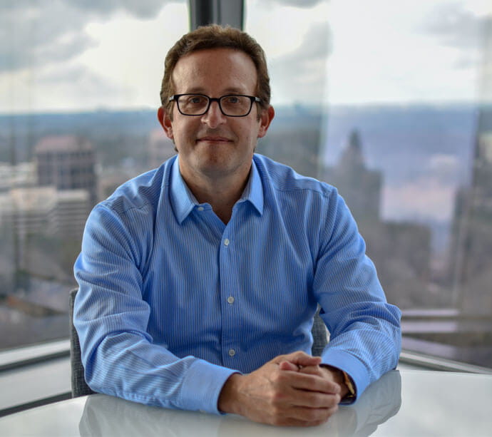 Man with glasses sitting at a desk with hands clasped near a city view, Jeff Sloan, Global Payments CEO