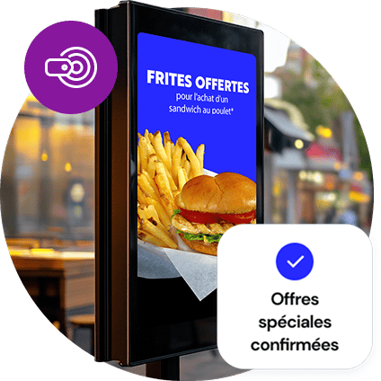 Un panneau numérique extérieur affiche une offre spéciale de frites gratuites. Un petit cercle violet avec une icône de prix recouvre l’image en haut et un encadré indiquant “Spéciaux confirmés” recouvre le bas de l’image.