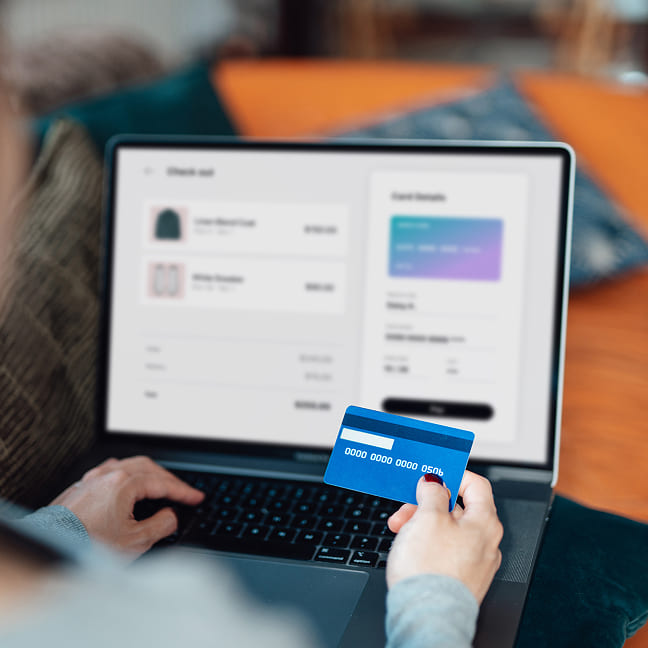 Egy személy kék bankkártyát tart a kezében, miközben laptopot használ online fizetéshez.