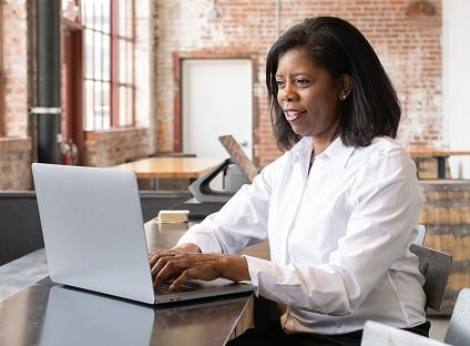 A woman sits at a table and types on the laptop in front of her.