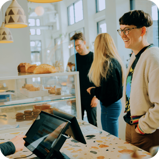 Customers stand in line to pay at a bakery, as a cashier types on a payment terminal.
