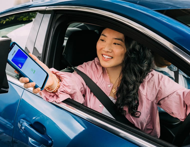 Woman smiling while using contactless payment with her phone in a drive=thru