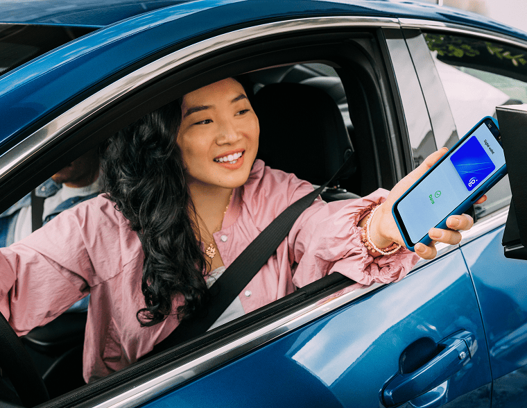 Woman smiling while using contactless payment with her phone in a drive=thru
