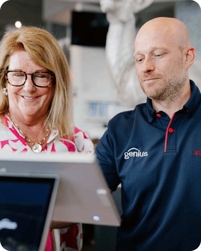 Man with Genius shirt talking with a woman in front of a terminal