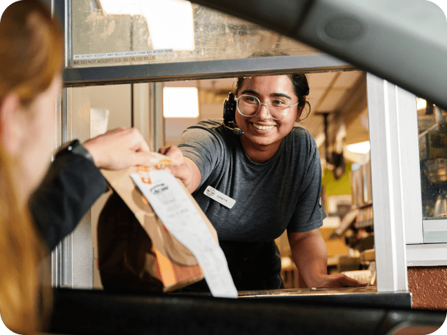 Quick service restaurant employee handing food to a customer in the drive thru