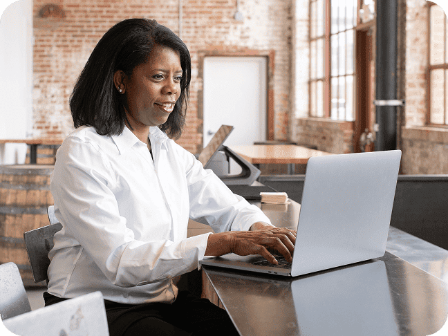 Woman sitting at counter in restaurant smiling and typing on a laptop computer