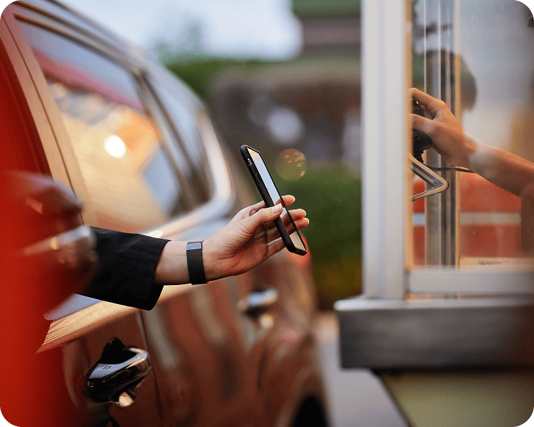 A quick service employee accepts a customer’s mobile payment in the drive thru.