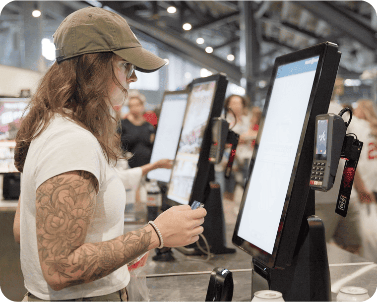 A woman holds a credit card while standing in front of a self-ordering kiosk in a large venue.