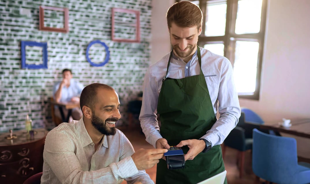 Waiter holding POS terminal for a customer paying with a credit card.