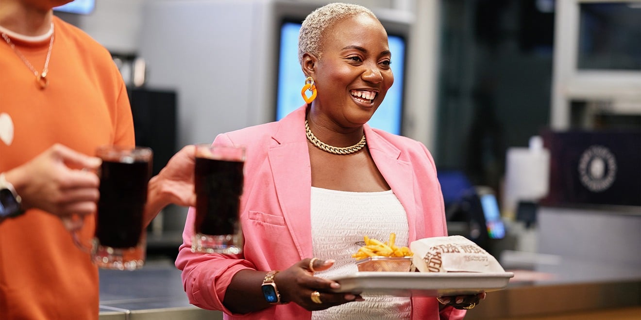 A cafeteria customer carries a tray of food through a dining hall.