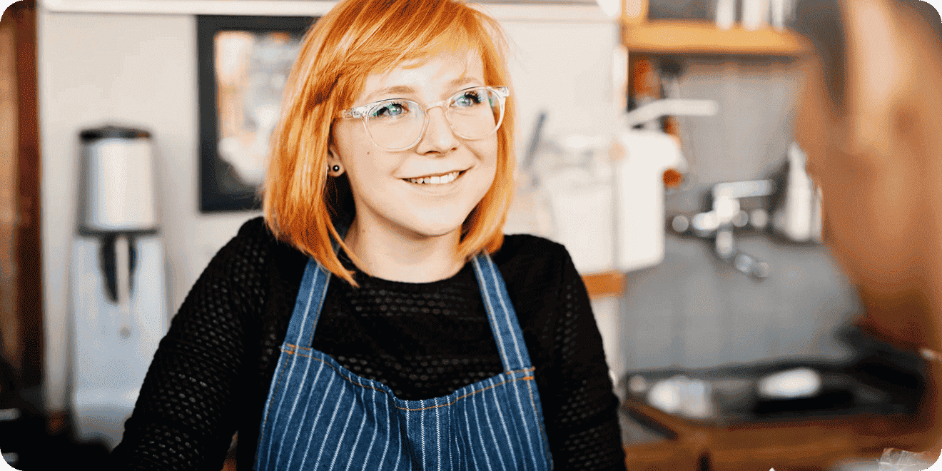 A barista wearing glasses welcomes a customer