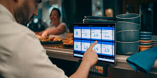 Person utillizing KDS in busy restaurant kitchen