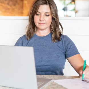 Small business owner with a slight smile looking down at laptop and taking notes