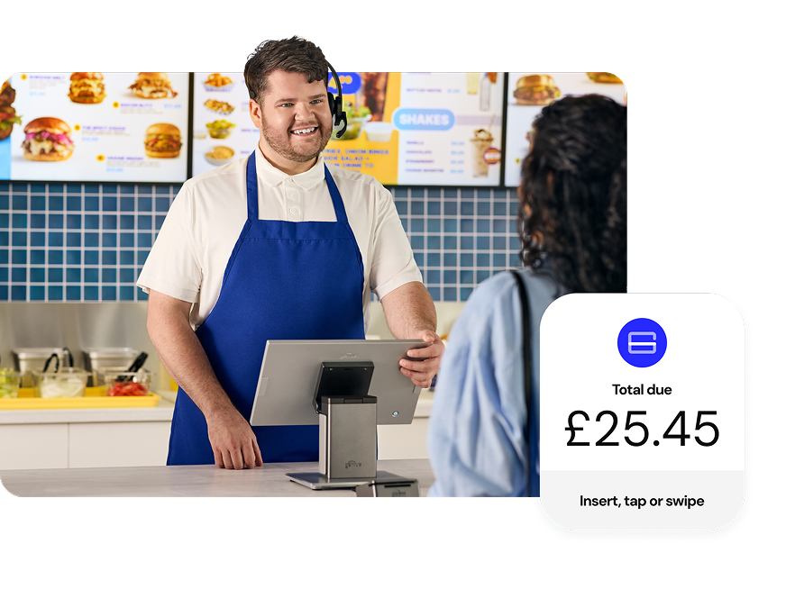 Smiling QSR employee taking a customer’s order on a Genius countertop POS while standing in front of digital menu boards
