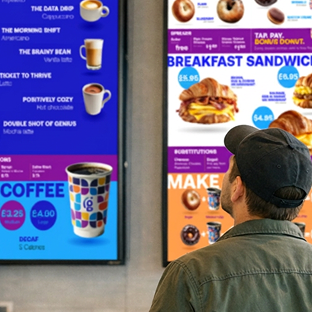 Coffee shop customer facing away from the camera looking up at Genius digital menu boards for cafes