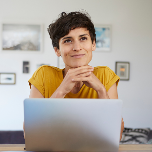 Smiling small business owner sitting in a home office in front of their open laptop