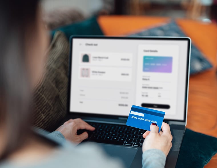 Person holding a blue credit card while using a laptop for online payment.