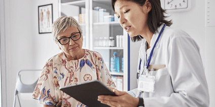 Doctor showing medical results on a tablet to a senior patient in a clinic.
