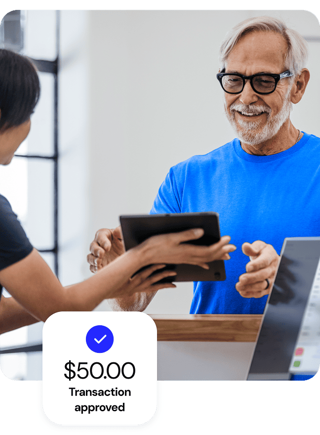 Senior man approving payment on a tablet with a $50.00 transaction approved overlay.